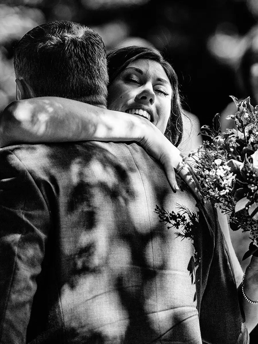 Bride smiling with eyes closed hugging her new husband tightly after the ceremony in black and white — documentary wedding photography by Gary Phillip