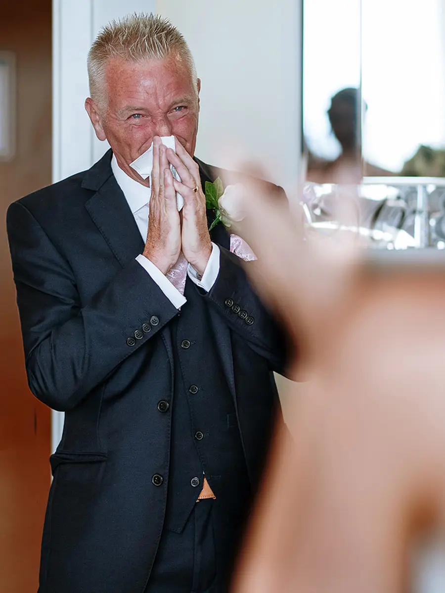 Father of the bride overcome with emotion pressing a handkerchief to his face as his daughter approaches — documentary wedding photography by Gary Phillip