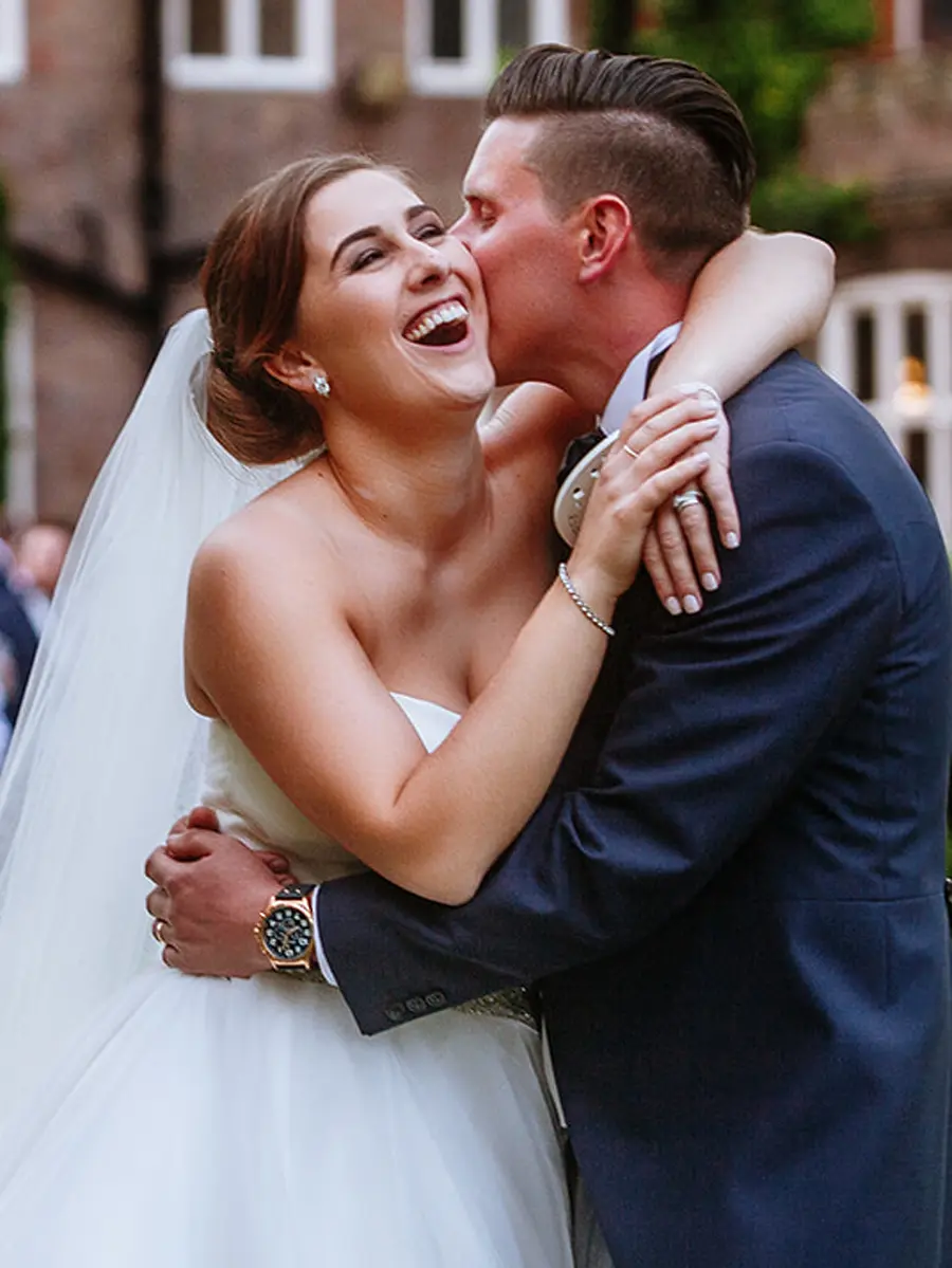Groom kissing his bride on the cheek as she laughs with pure joy outside their wedding venue — documentary wedding photography by Gary Phillip