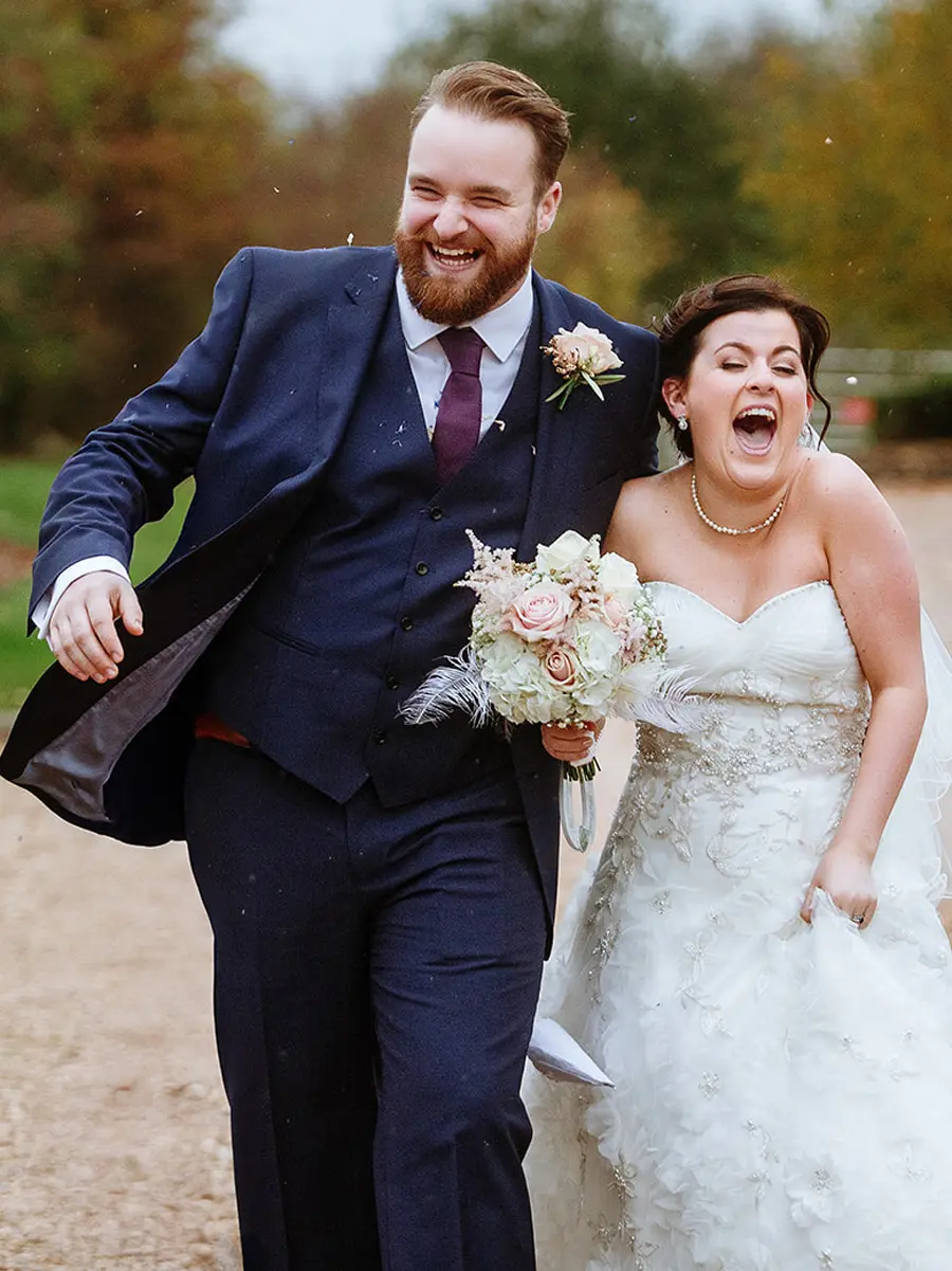 Bride and groom walking and laughing together down a country lane in autumn, both unable to contain their joy — documentary wedding photography by Gary Phillip