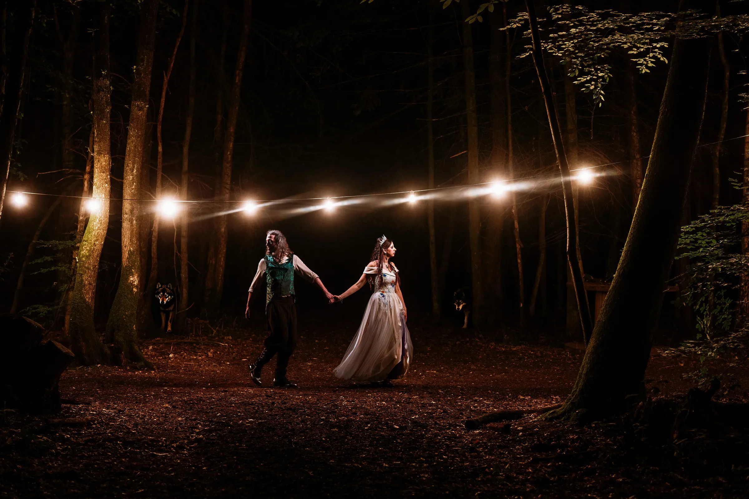 A couple standing in a Kent forest at night beneath string lights, wolves watching from the darkness — wedding photography by Gary Phillip