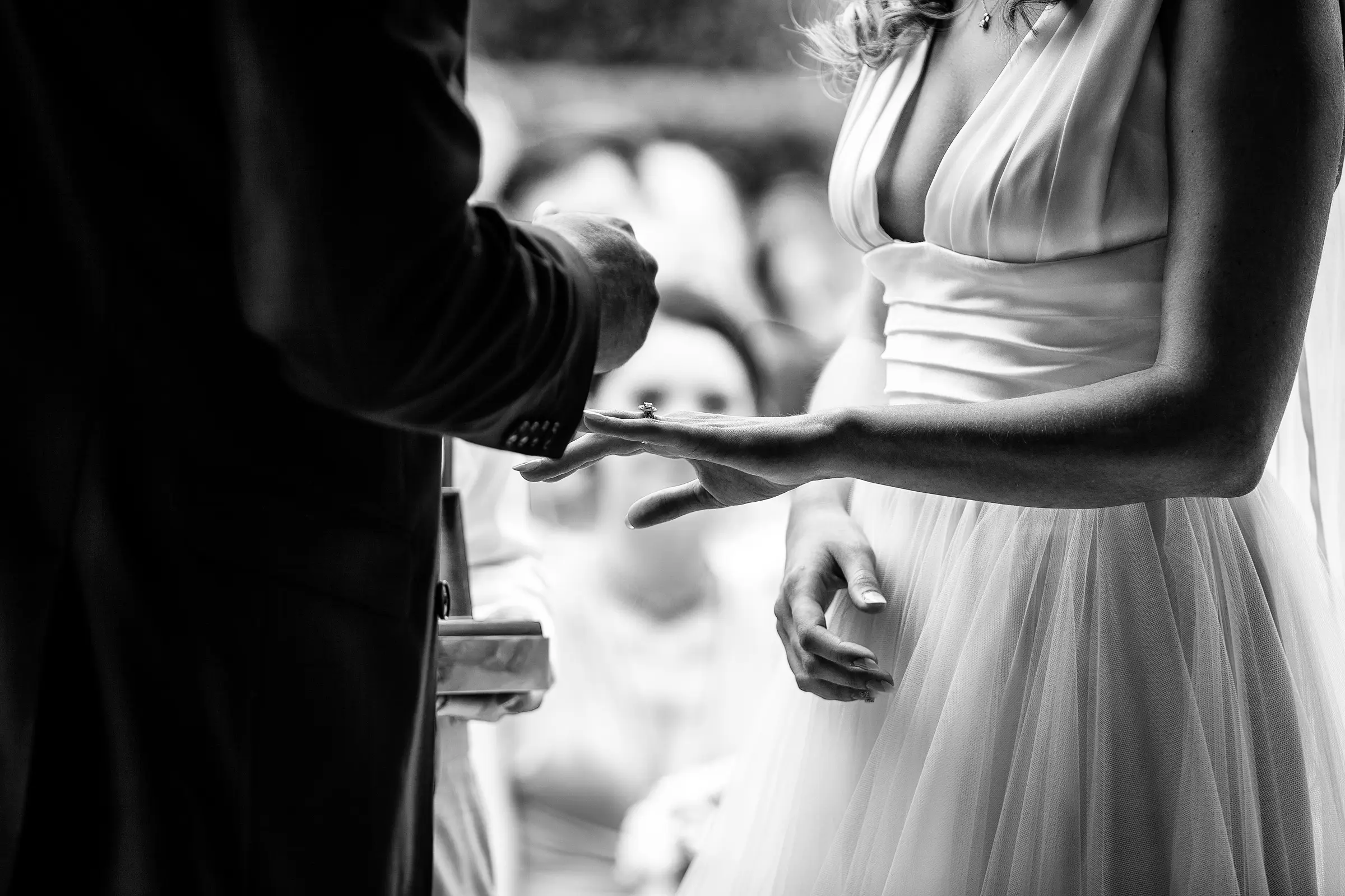 Close up of groom placing the wedding ring on the bride's finger during the ceremony, guests watching in soft focus behind them — documentary wedding photography by Gary Phillip