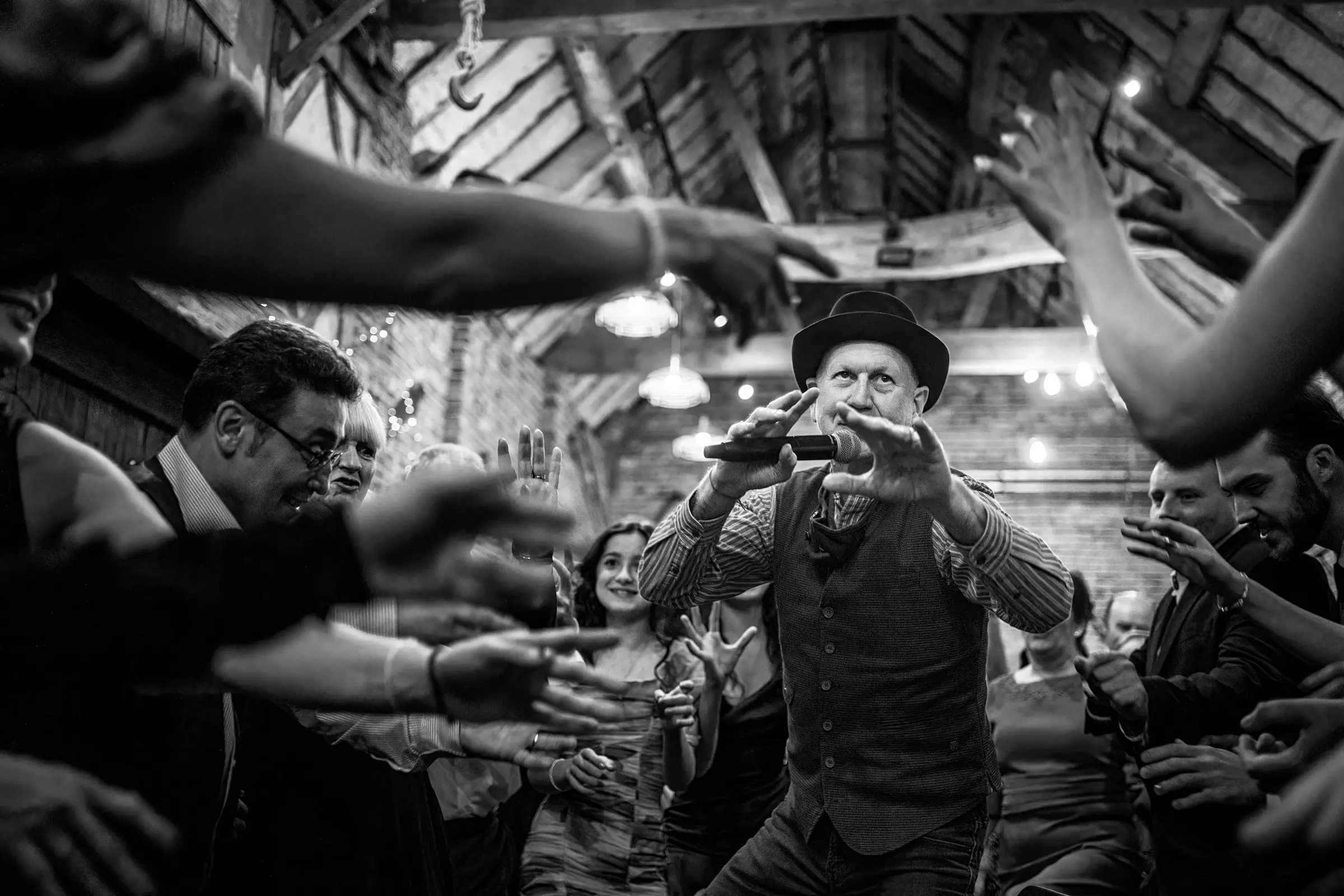 Cèilidh wedding band instructing a full dance floor at a packed donington park farmhouse, surrounded by reaching hands and dancing guests, shot from the dancefloor looking up — documentary wedding photography by Gary Phillip