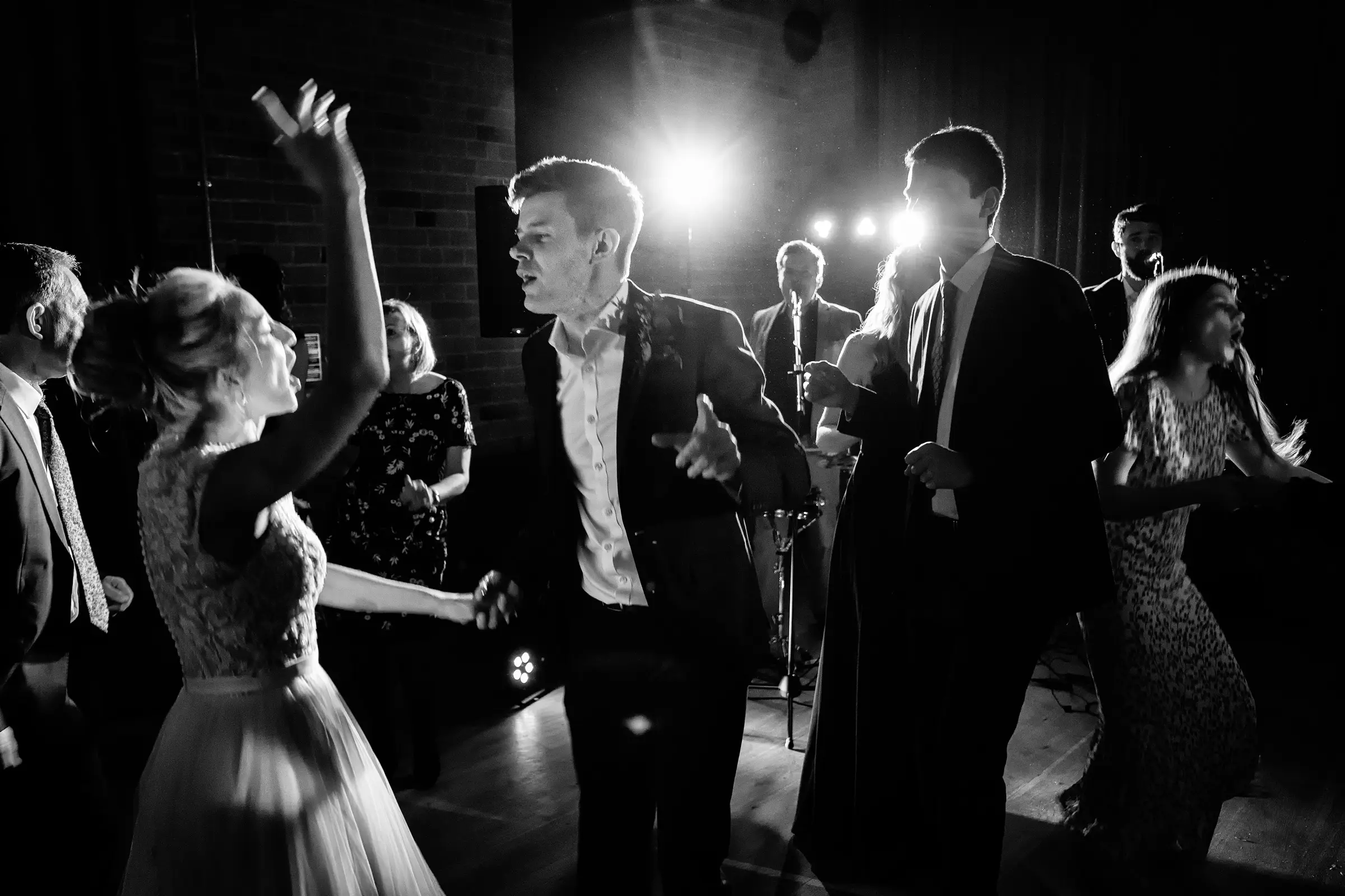 Bride and groom dancing together on the dancefloor in black and white, live band performing behind them in the spotlight — documentary wedding photography by Gary Phillip