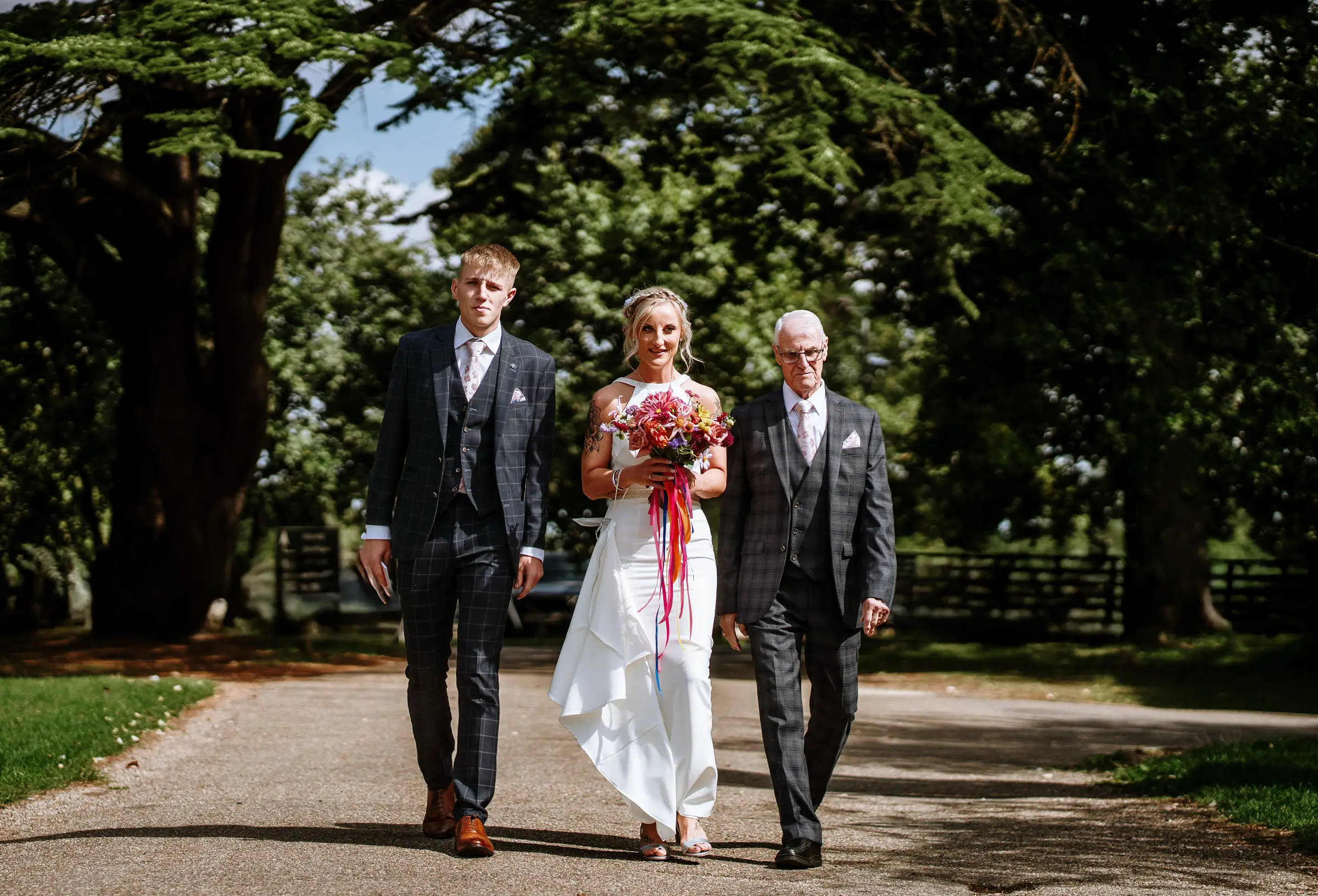 Bride Amy arriving with her father and son walking down the drive to the coach house at Doddington Hall, Lincolnshire on her wedding day