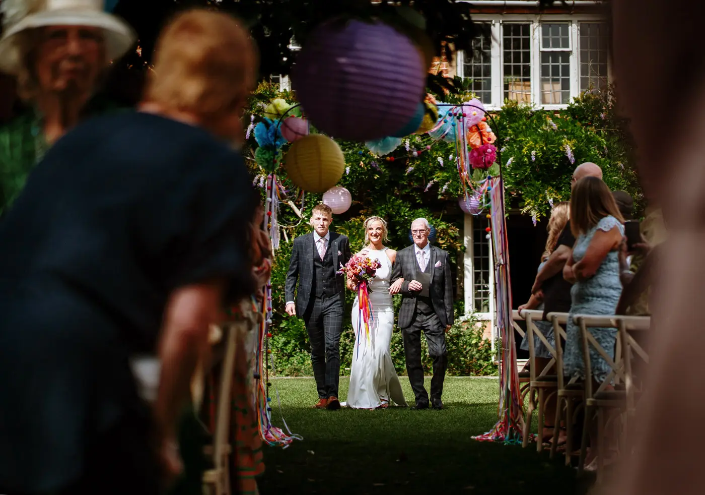 Bride Amy arriving at the head of the aisle at Doddington Hall accompanied by her father and son, all smiling as they approach Abby