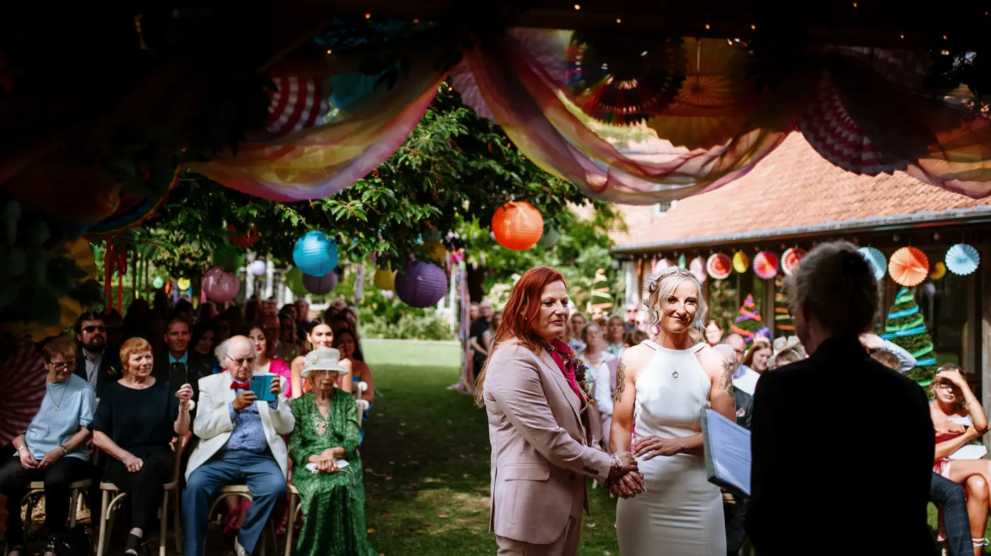 Amy and Abby with their registrar during the wedding ceremony at Doddington Hall with smiling guests visible behind them