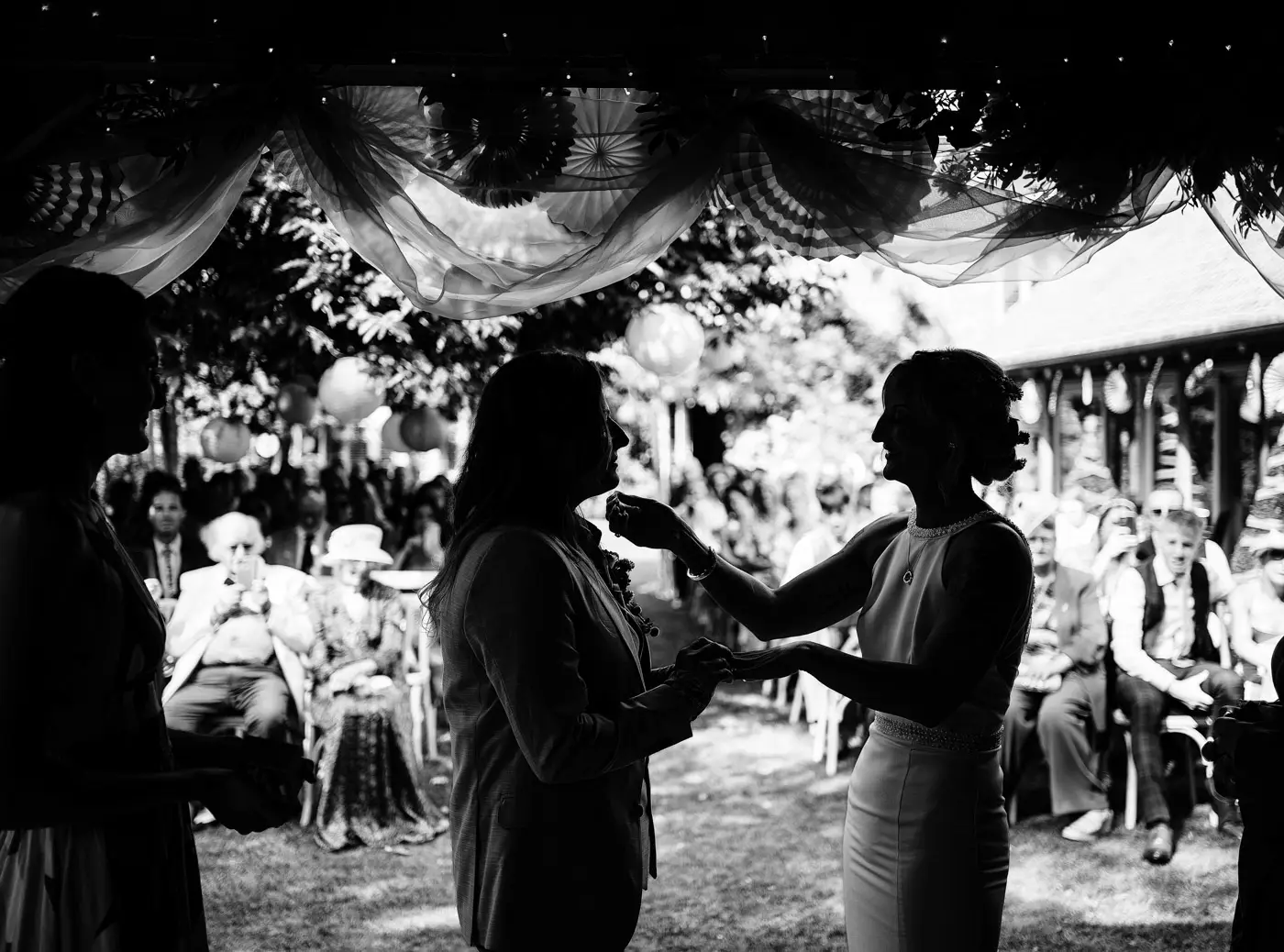 Black and white silhouette of Amy and Abby with wedding guests behind them during the ceremony at Doddington Hall, Lincolnshire