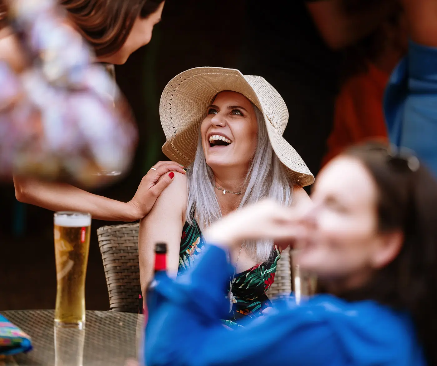 A guest in a floppy hat laughing in the coach house garden at Doddington Hall during Amy and Abby's wedding reception, Lincolnshire