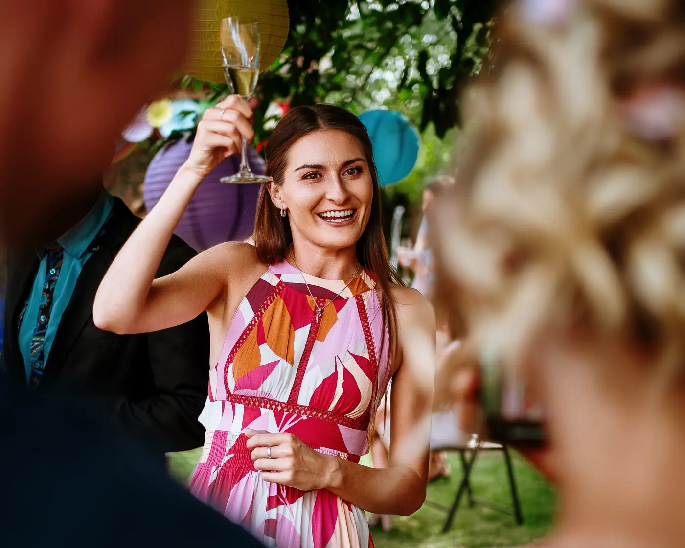 A guest raising her glass of champagne in a toast with other guests in the garden at Doddington Hall, Lincolnshire during Amy and Abby's wedding