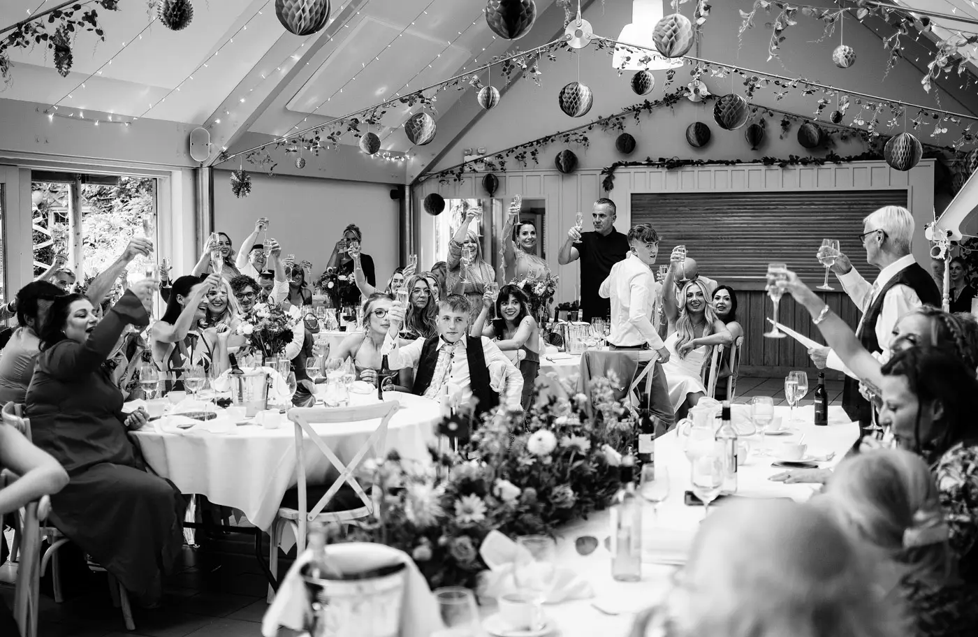Black and white image of the whole room raising a glass to Amy and Abby during the wedding speeches at Doddington Hall, Lincolnshire