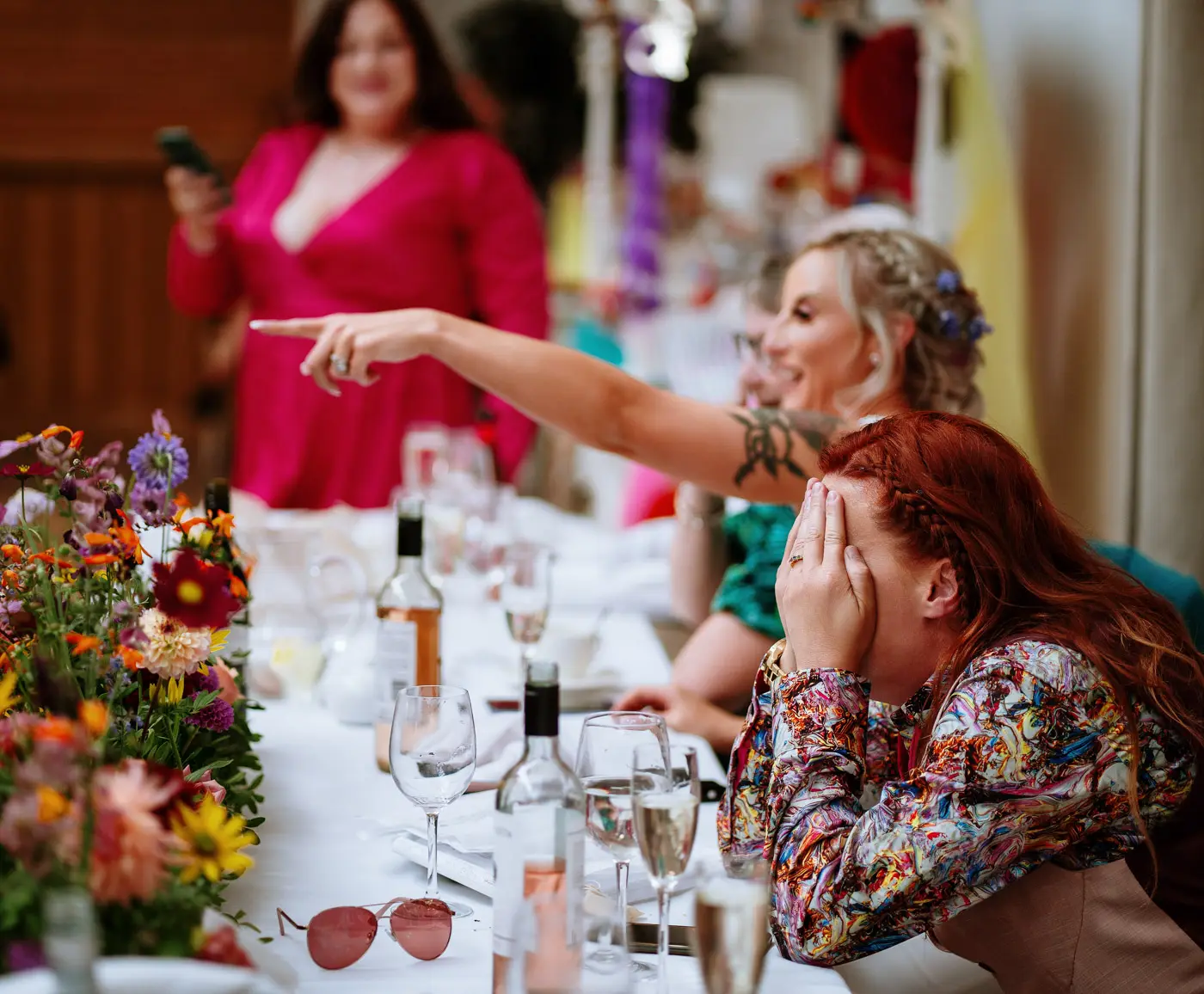 Abby covering her face in embarrassment during the best woman's speech while Amy points out the culprit at Doddington Hall, Lincolnshire