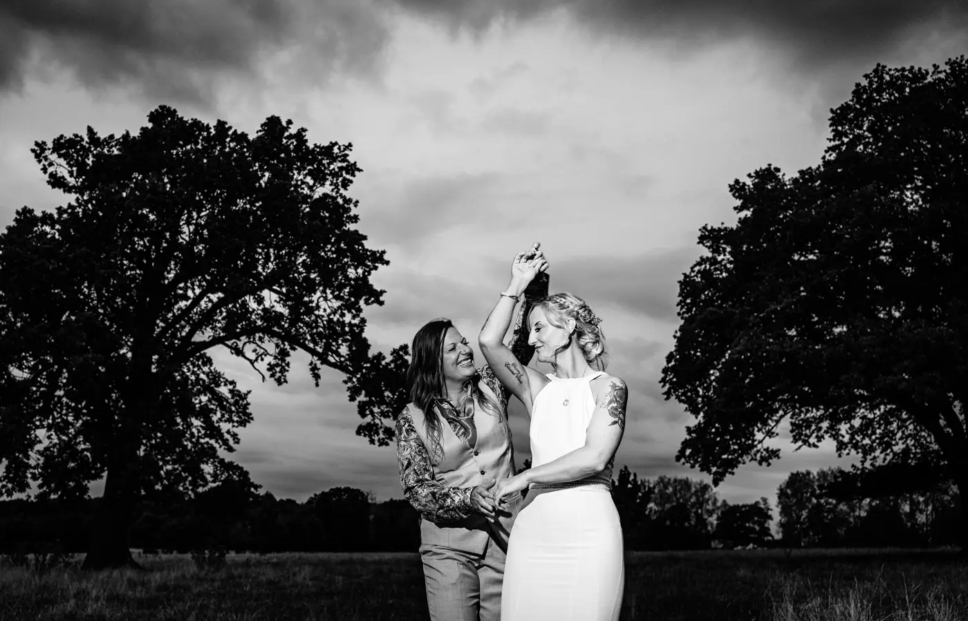 Black and white portrait of Amy and Abby in a field at Doddington Hall, Lincolnshire, Abby spinning Amy between two trees in a beautiful evening moment