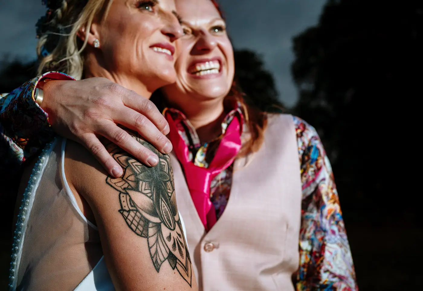 Close up of Amy and Abby laughing together at Doddington Hall, Lincolnshire, with Amy's arm tattoo as the focal point, documentary wedding photography by Gary Phillip
