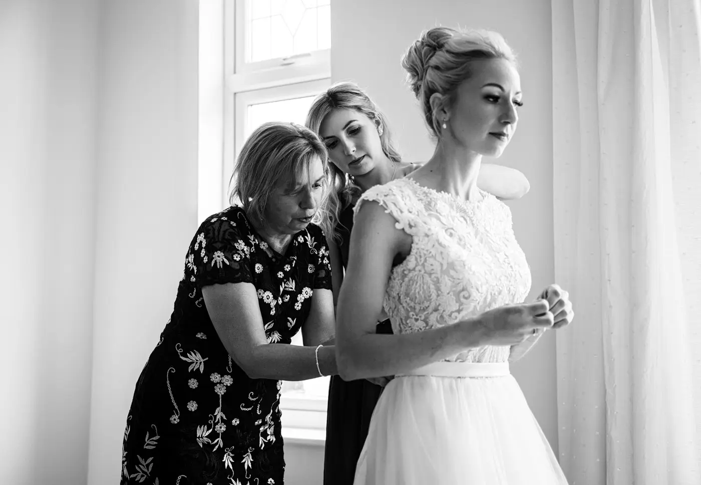 Bride Ellen being helped into her wedding dress by her mum and chief bridesmaid on her wedding morning in Nottinghamshire