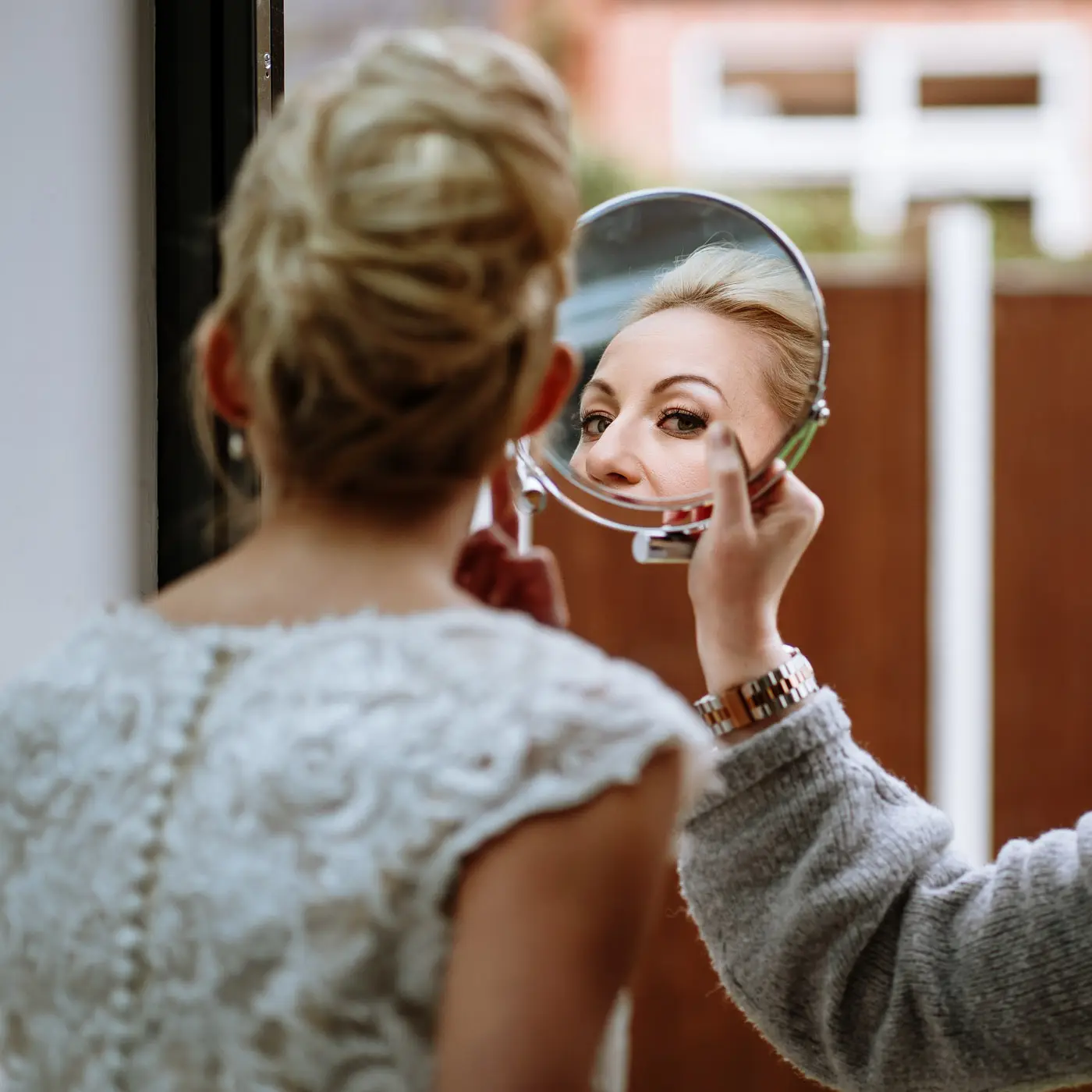 Bride Ellen seeing her finished look in a mirror held by her makeup artist on the morning of her wedding at Carriage Hall, Nottinghamshire
