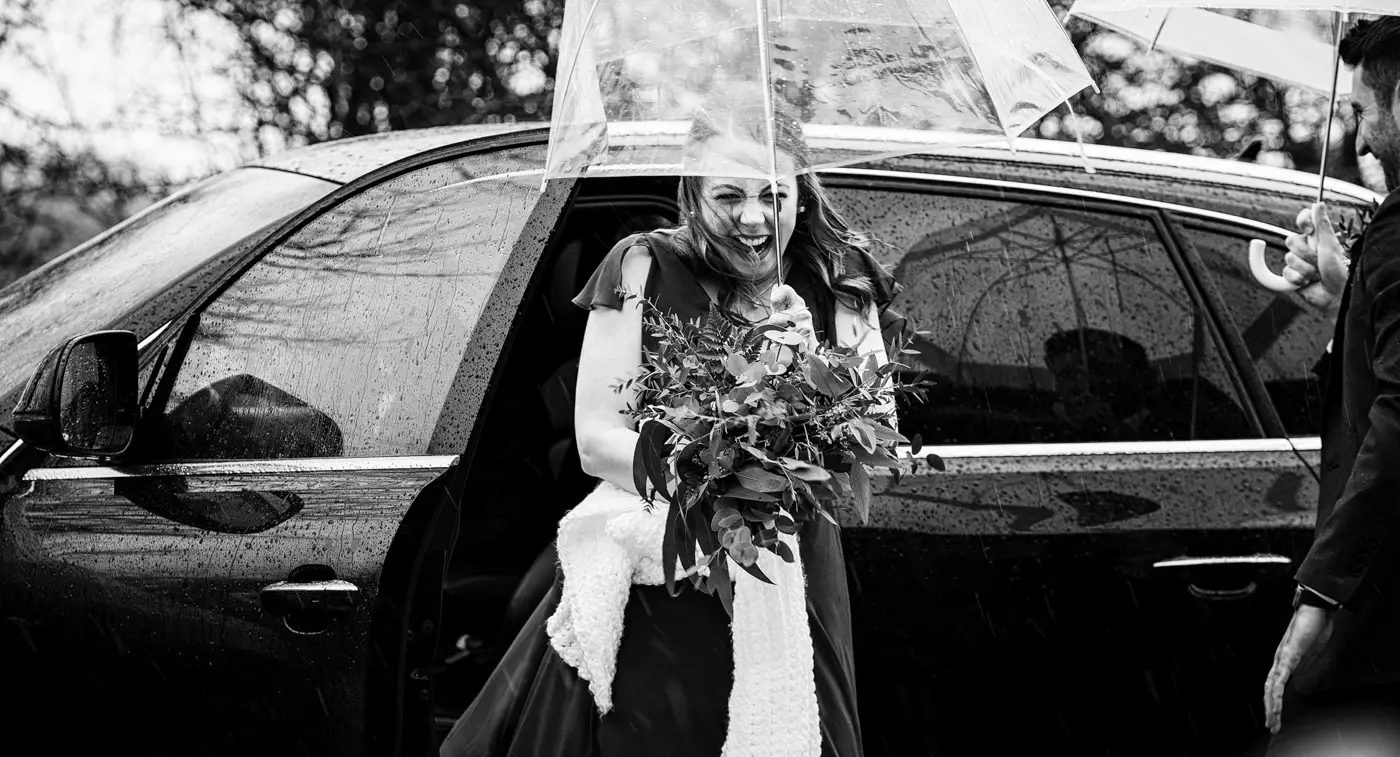 Bridesmaids emerging from the wedding car under a brolly as the rain hammers down on Ellen and Ben's February wedding day at Carriage Hall