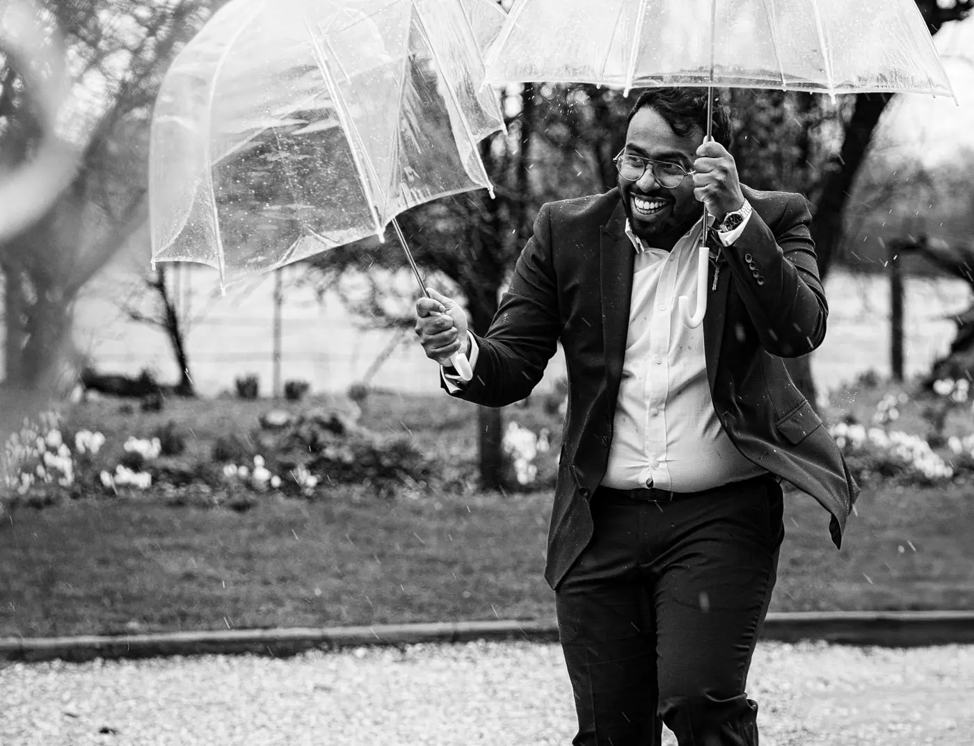 Best man holding two umbrellas to help guests arrive in the rain at Carriage Hall, Nottinghamshire for Ellen and Ben's winter wedding