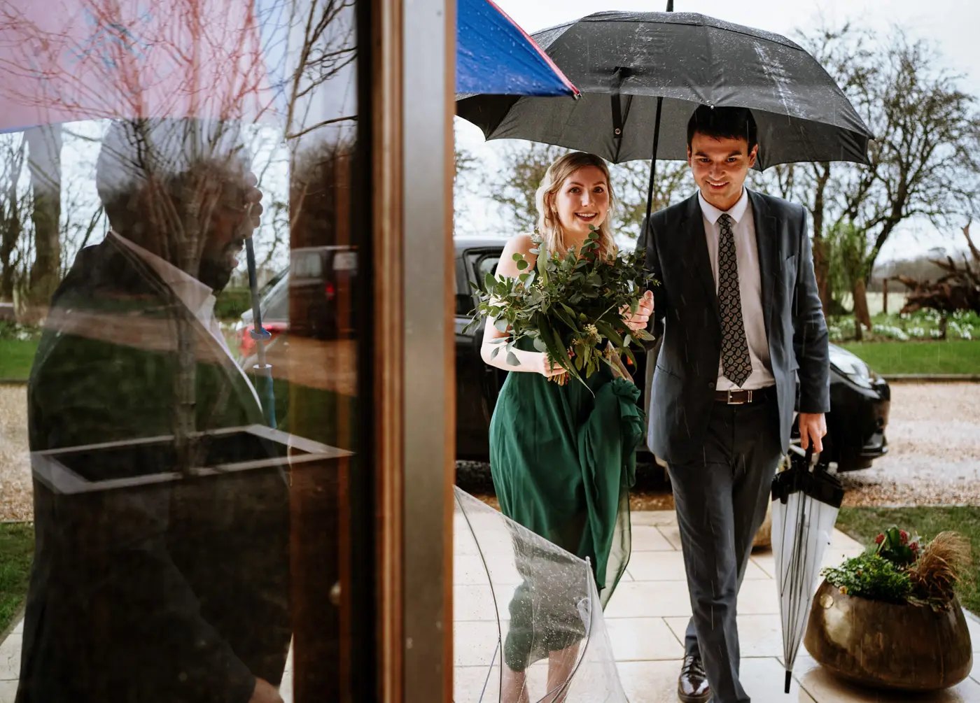 Wedding guests sharing a brolly as they arrive together at Carriage Hall for Ellen and Ben's February wedding in Nottinghamshire