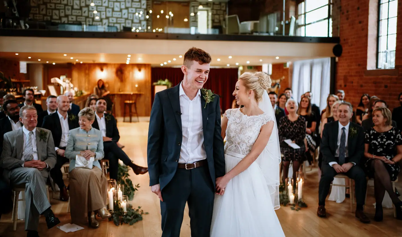 Bride Ellen and groom Ben laughing as the sausage dog ring bearer is led away to the guests during their ceremony at Carriage Hall