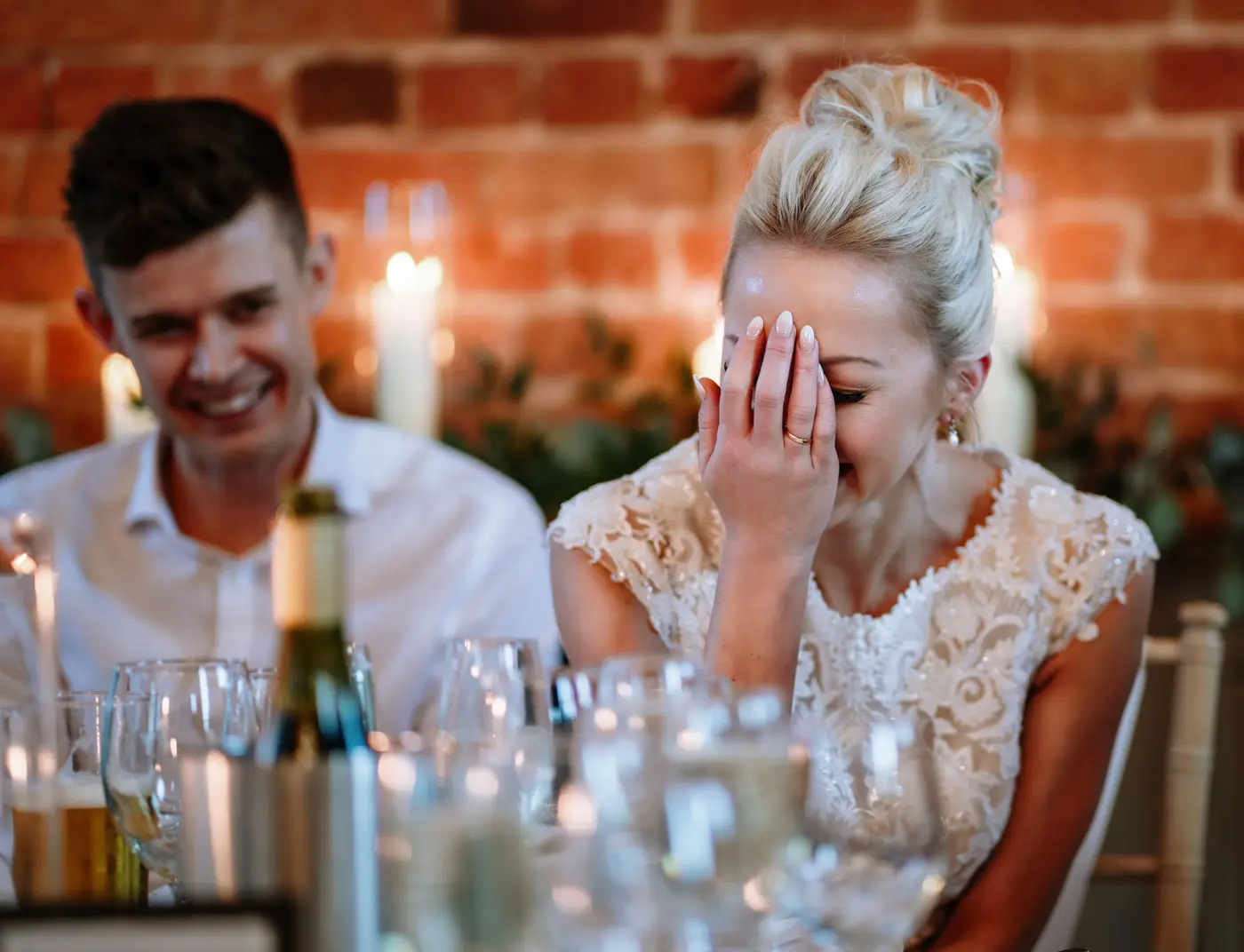 Bride Ellen covering her face with embarrassment while groom Ben looks on smiling during the speeches at Carriage Hall, Nottinghamshire