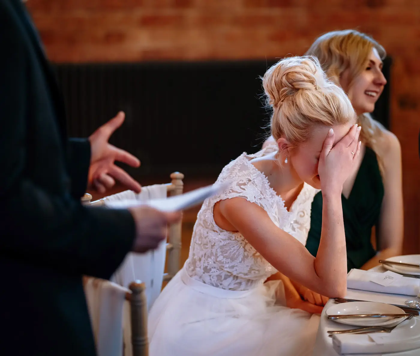 Bride Ellen covering her face again with laughter during the wedding speeches at Carriage Hall, Nottinghamshire