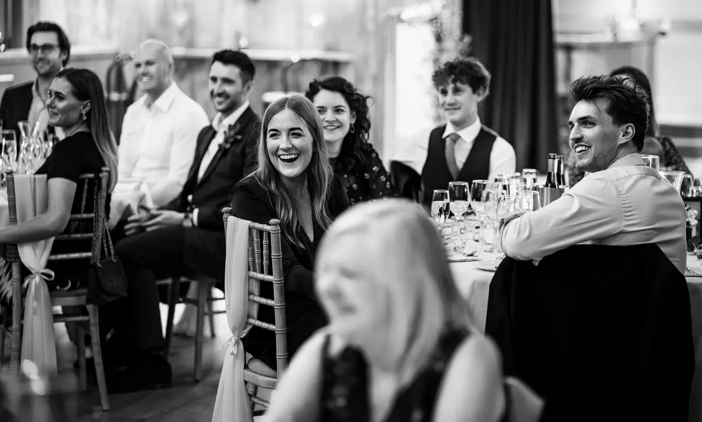 Black and white image of wedding guests all looking on and laughing during the speeches at Carriage Hall, Nottinghamshire
