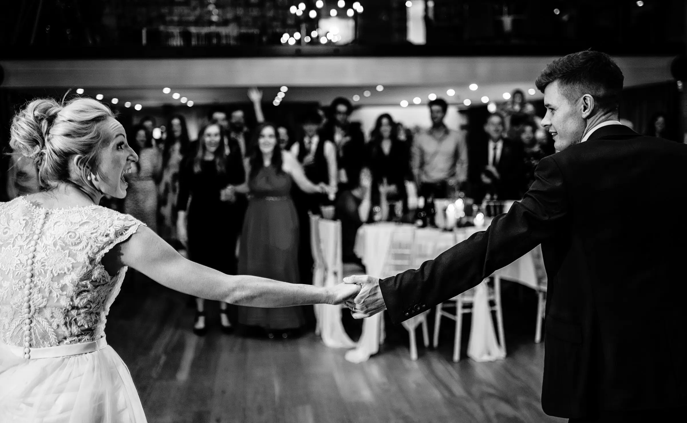 Ellen and Ben's first dance with outstretched arms looking at each other while their guests watch on in the background at Carriage Hall, Nottinghamshire
