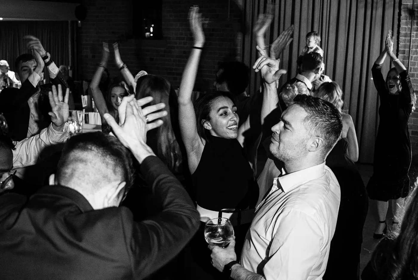 Black and white image of wedding guests with arms in the air loving every moment of the evening at Carriage Hall, Nottinghamshire