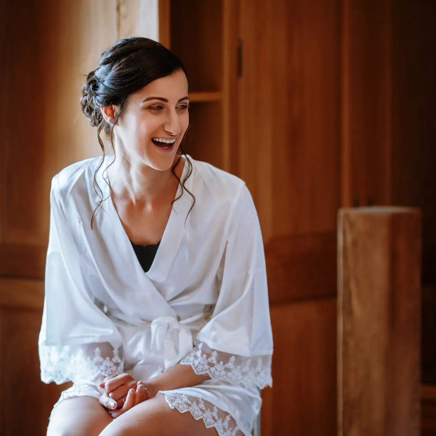 Bride Krissie seated and laughing in her dressing gown during wedding morning preparations at Swancar Farm, honest candid wedding photography by Gary Phillip
