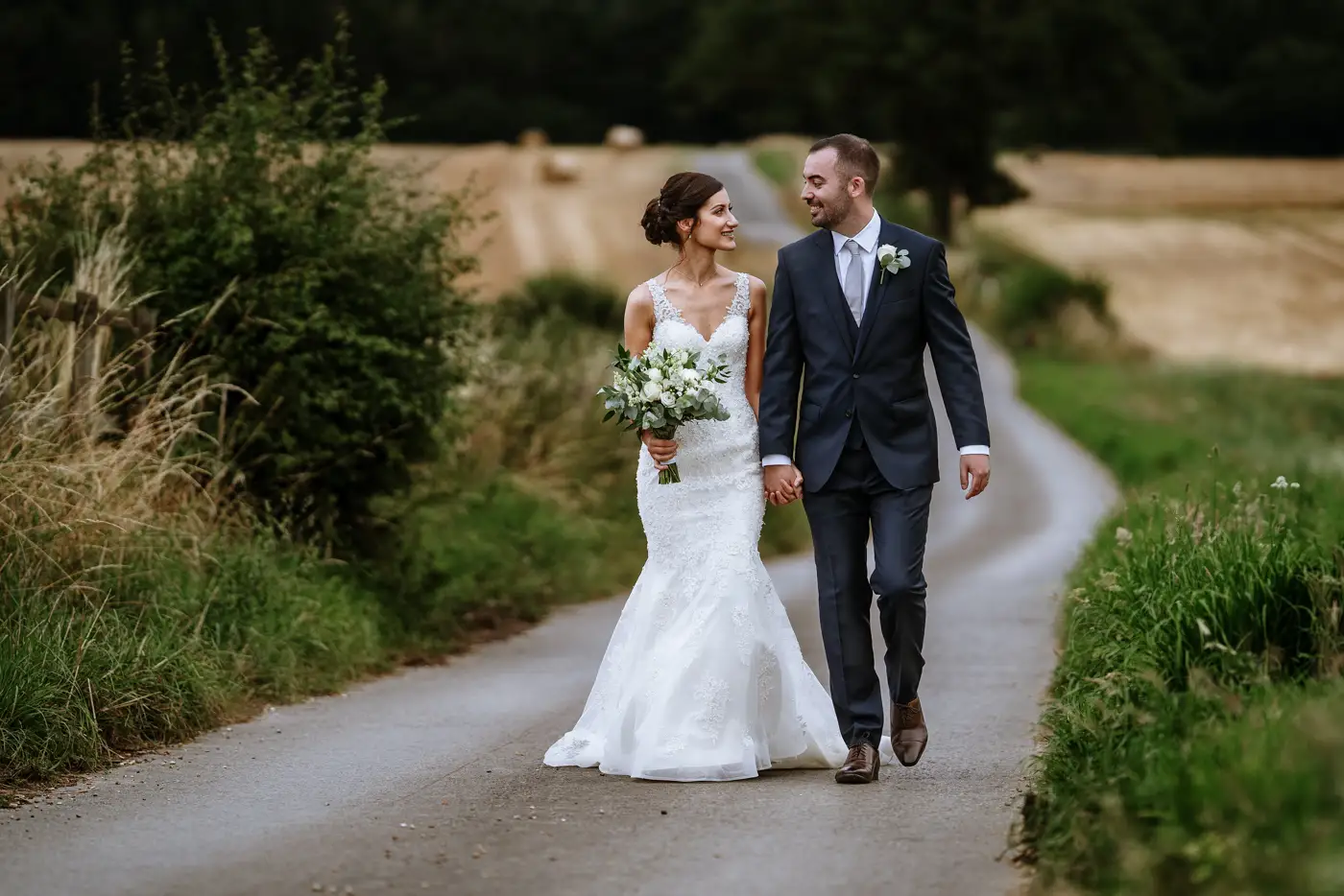 Bride Krissie and groom Tom walking together along Swancar Farm's long tree-lined road, documentary wedding photography by Gary Phillip, Nottingham