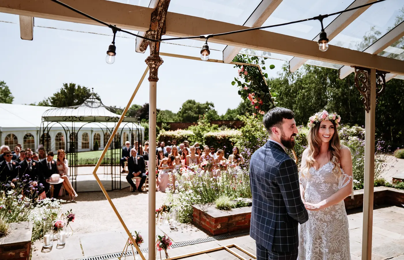 Laura and Gavin standing at the front with the registrar while their guests are seated behind and the sun cracks the flagstones at Beeston Fields, Nottingham