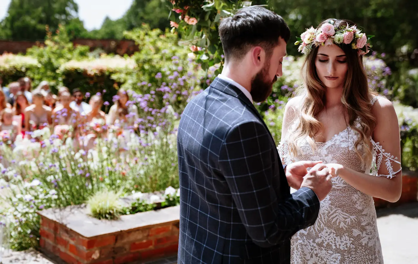 Groom Gavin placing the wedding ring on bride Laura's finger during their ceremony at The Walled Garden at Beeston Fields, Nottingham