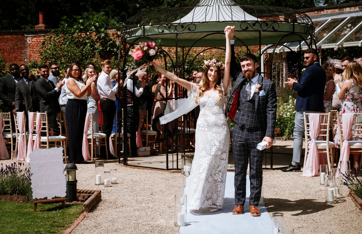 Bride Laura and groom Gavin celebrating with their hands aloft after tying the knot at The Walled Garden at Beeston Fields, Nottingham