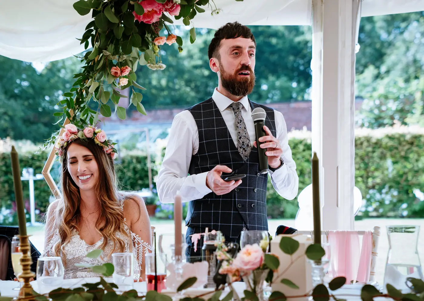 Groom Gavin delivering a serious-faced speech while bride Laura is in fits of giggles behind him at The Walled Garden at Beeston Fields, Nottingham