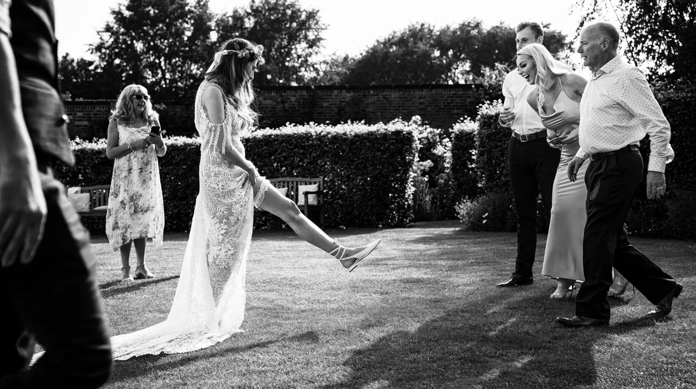 Bride Laura showing off her garter while guests laugh along at the wedding reception at The Walled Garden at Beeston Fields, Nottingham