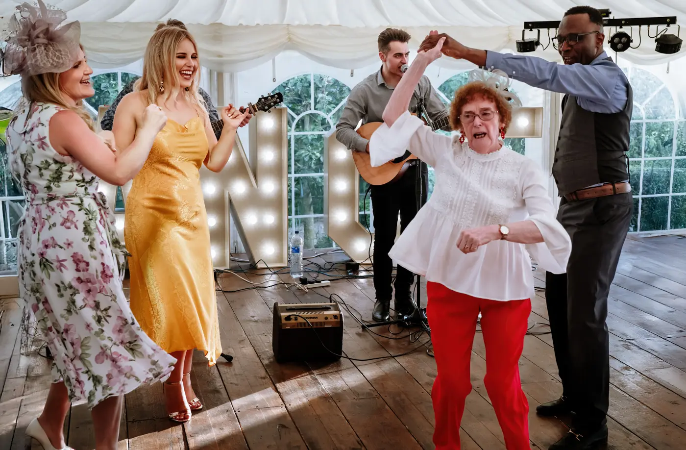 An elderly female guest in bright red trousers twirling on the dancefloor while other guests laugh along at The Walled Garden at Beeston Fields, Nottingham