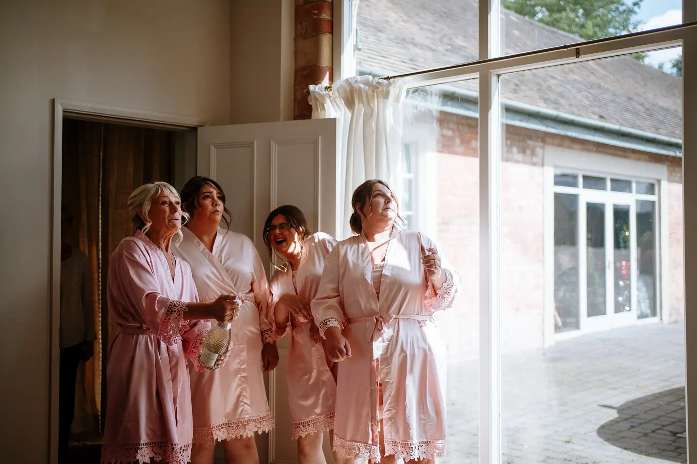 Bridesmaids and mother of the bride opening the champagne together on the morning of Louise and Martin's wedding at Doddington Hall