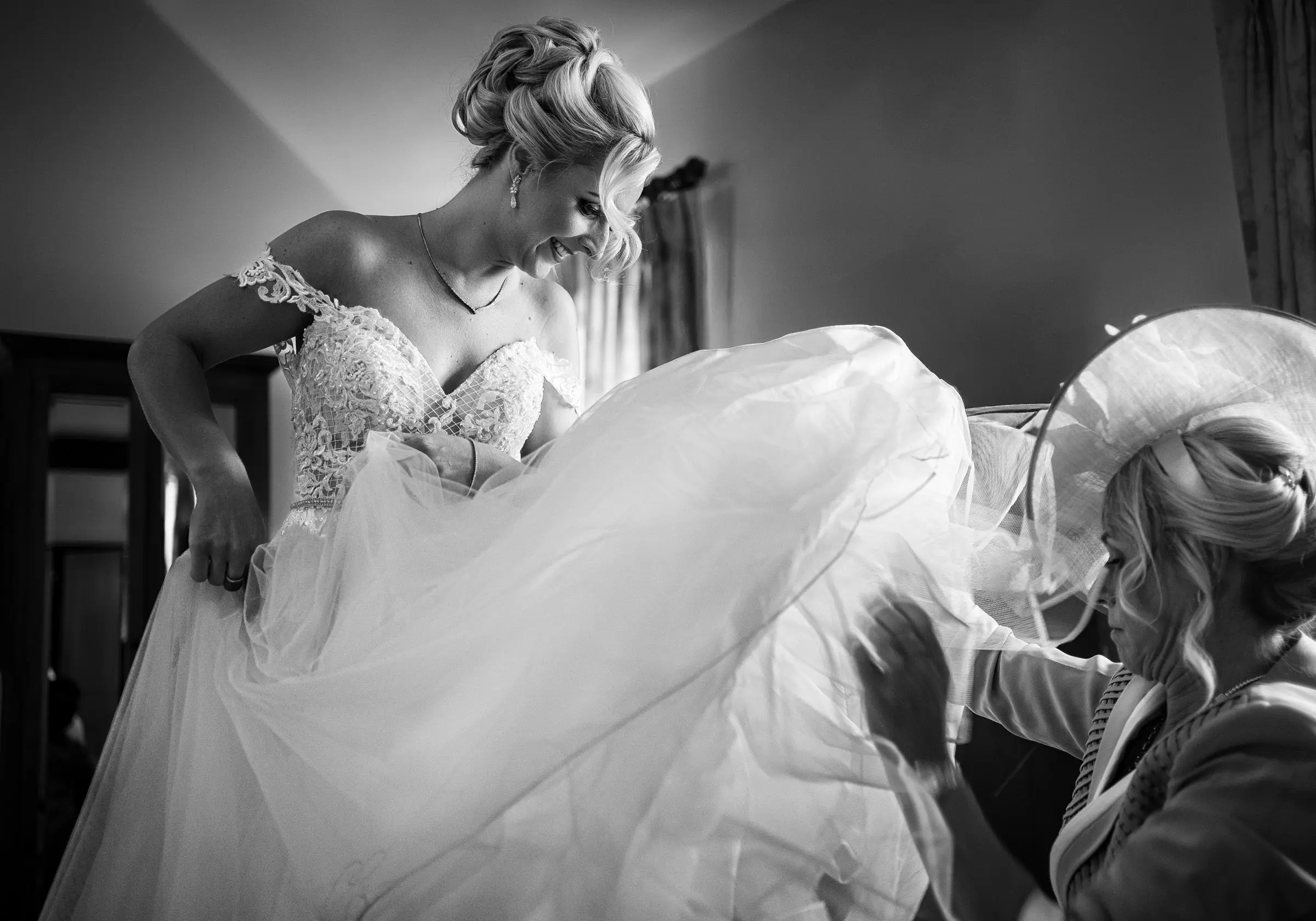 Black and white image of the mother of the bride helping bride Louise into her wedding dress at Doddington Hall, Lincolnshire