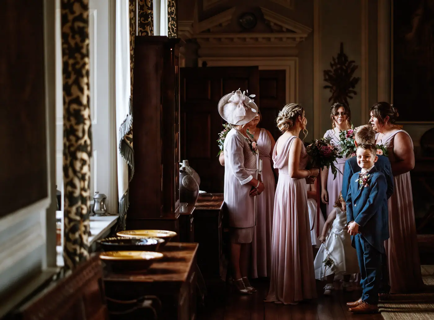 The bridal party waiting for bride Louise at Doddington Hall while the page boy gives the photographer a cheeky grin during the wedding ceremony preparations