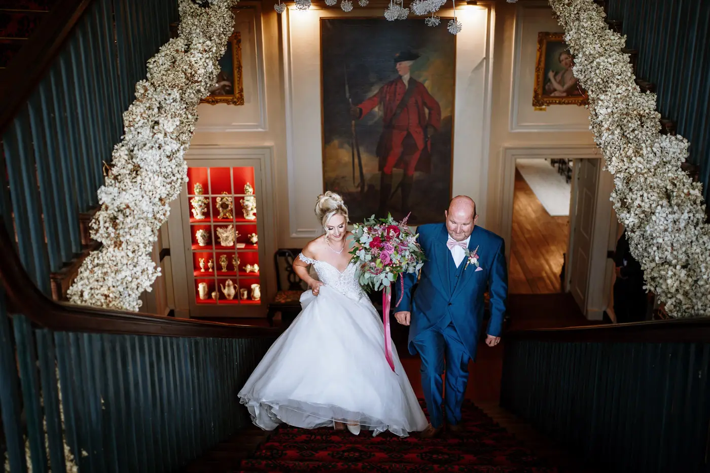 Bride Louise making her way up the grand staircase at Doddington Hall with her father by her side on her wedding day