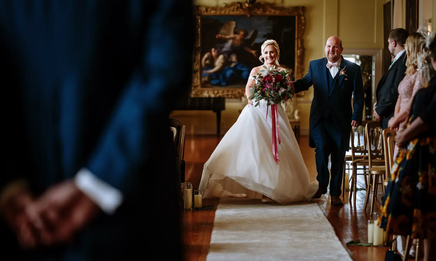 Bride Louise making her way down the aisle in the Long Gallery at Doddington Hall with her father, documentary wedding photography by Gary Phillip