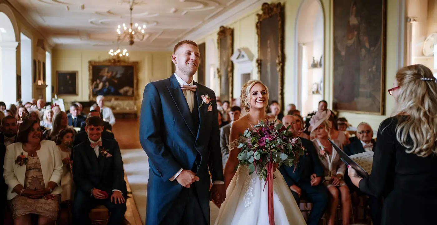 Bride Louise and groom Martin laughing together at the front of the Long Gallery at Doddington Hall during their wedding ceremony in Lincolnshire