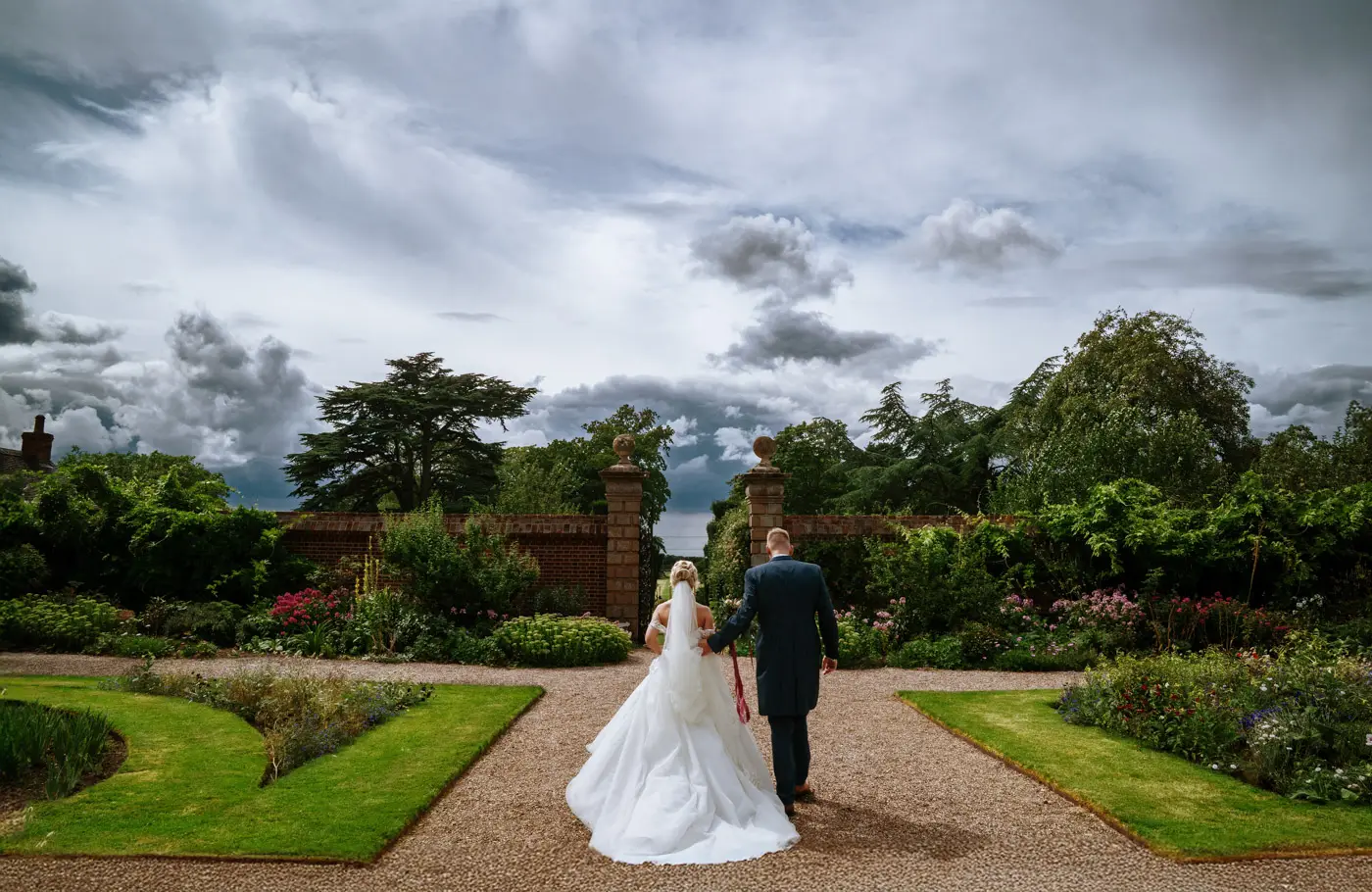 Bride Louise and groom Martin walking together through the beautiful gardens at Doddington Hall, Lincolnshire after their wedding ceremony