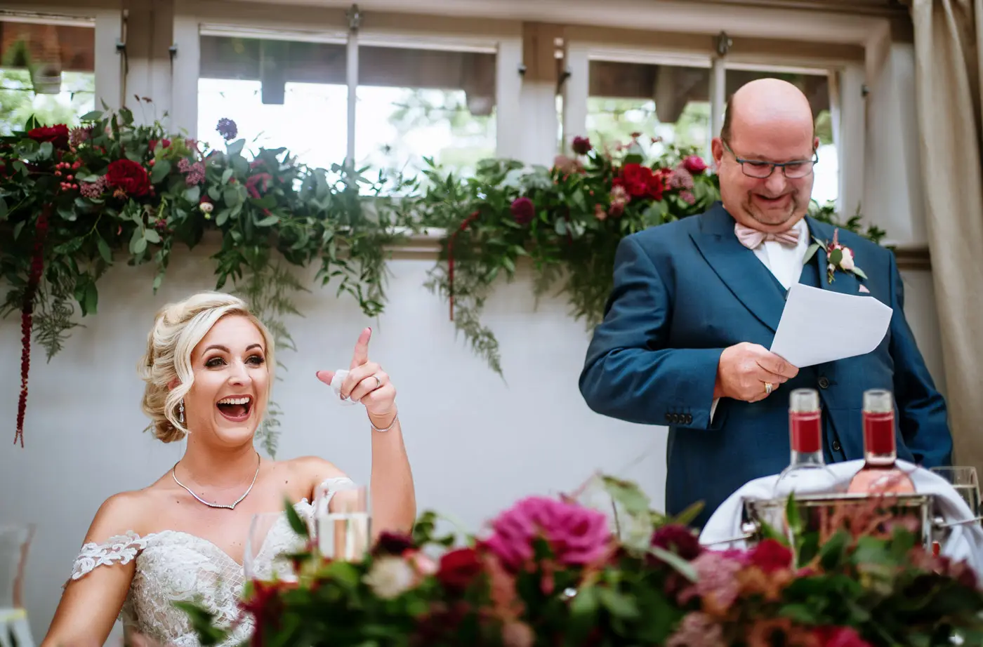 Bride Louise laughing and pointing at her guests during the wedding speeches at Doddington Hall, Lincolnshire