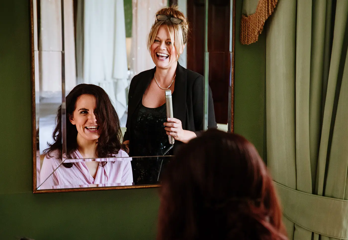 Bridesmaid laughing with the makeup artist while looking in the mirror at Stubton Hall, Nottinghamshire, candid wedding morning photography by Gary Phillip