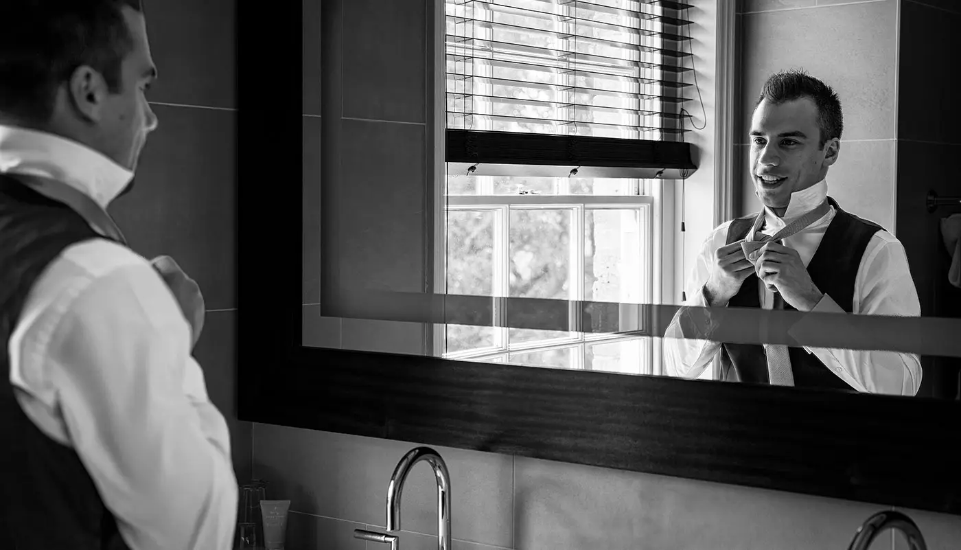 Groom Luke tying his tie in a bathroom mirror reflection at Stubton Hall on his wedding morning, a classic preparatory moment captured by Gary Phillip