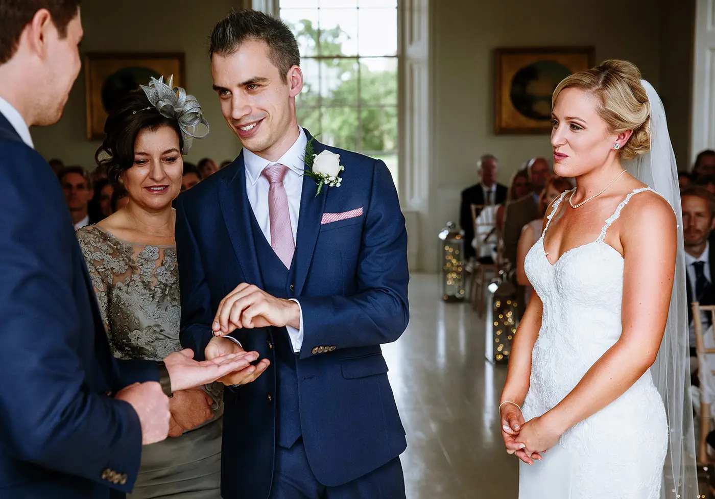 Groom Luke taking the wedding ring from his best man with a wry smile while bride Sally looks on during the ceremony at Stubton Hall, Nottinghamshire
