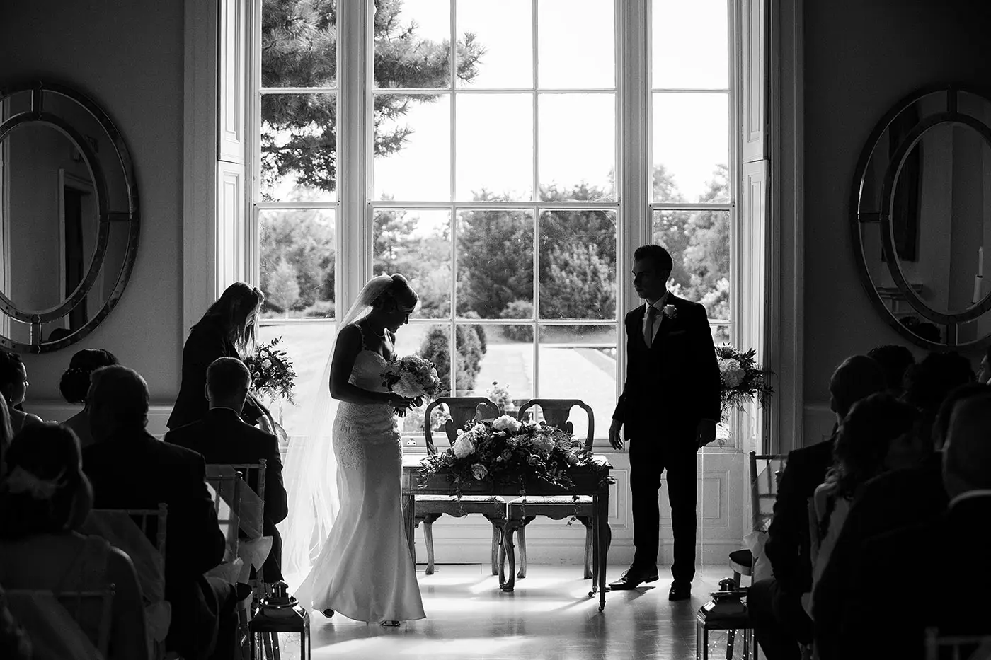 Black and white silhouette of bride Sally and groom Luke rising from the signing table with the grand window of Stubton Hall behind them