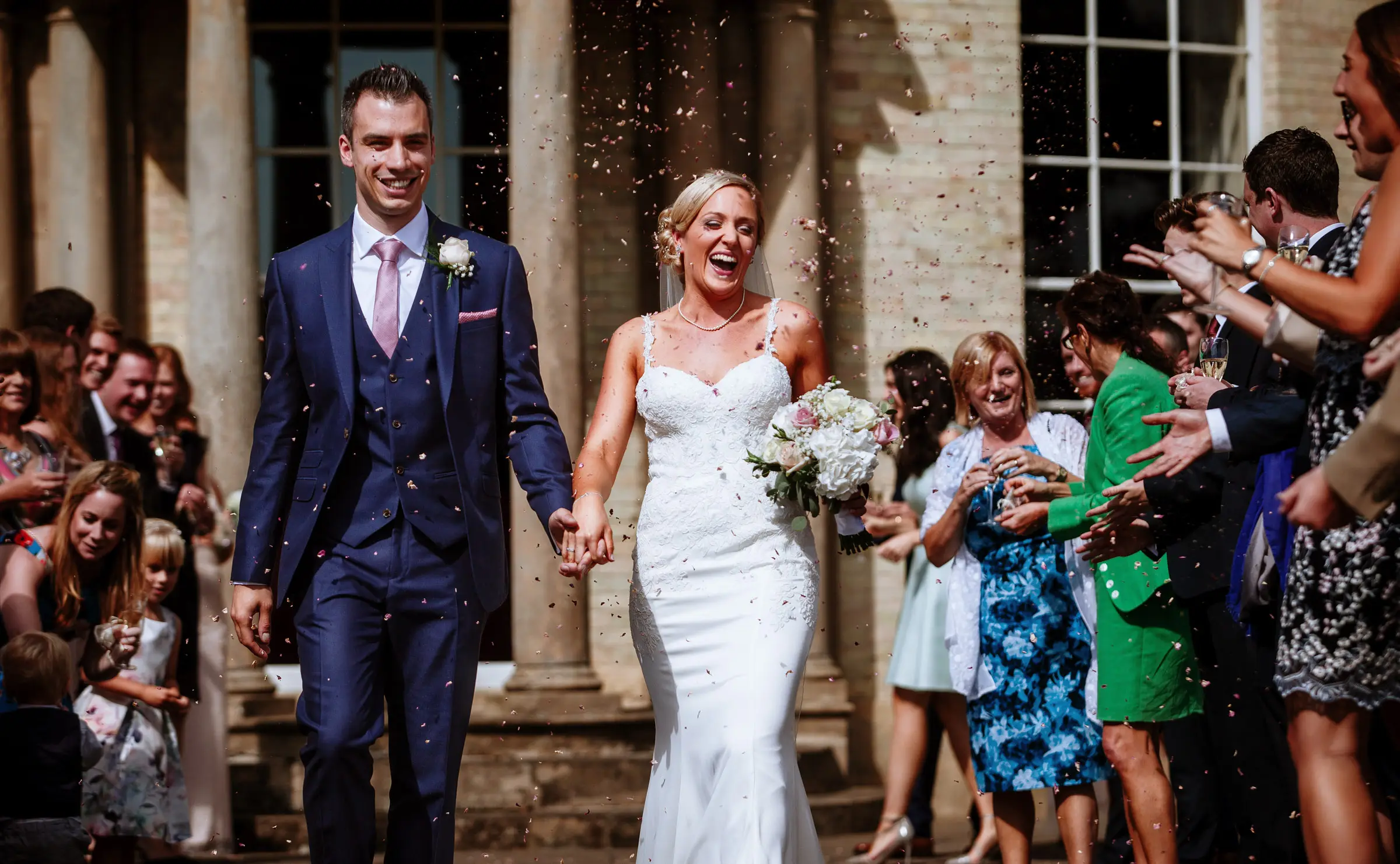 Bride Sally laughing with delight as she and groom Luke walk through a storm of confetti outside Stubton Hall, Nottinghamshire
